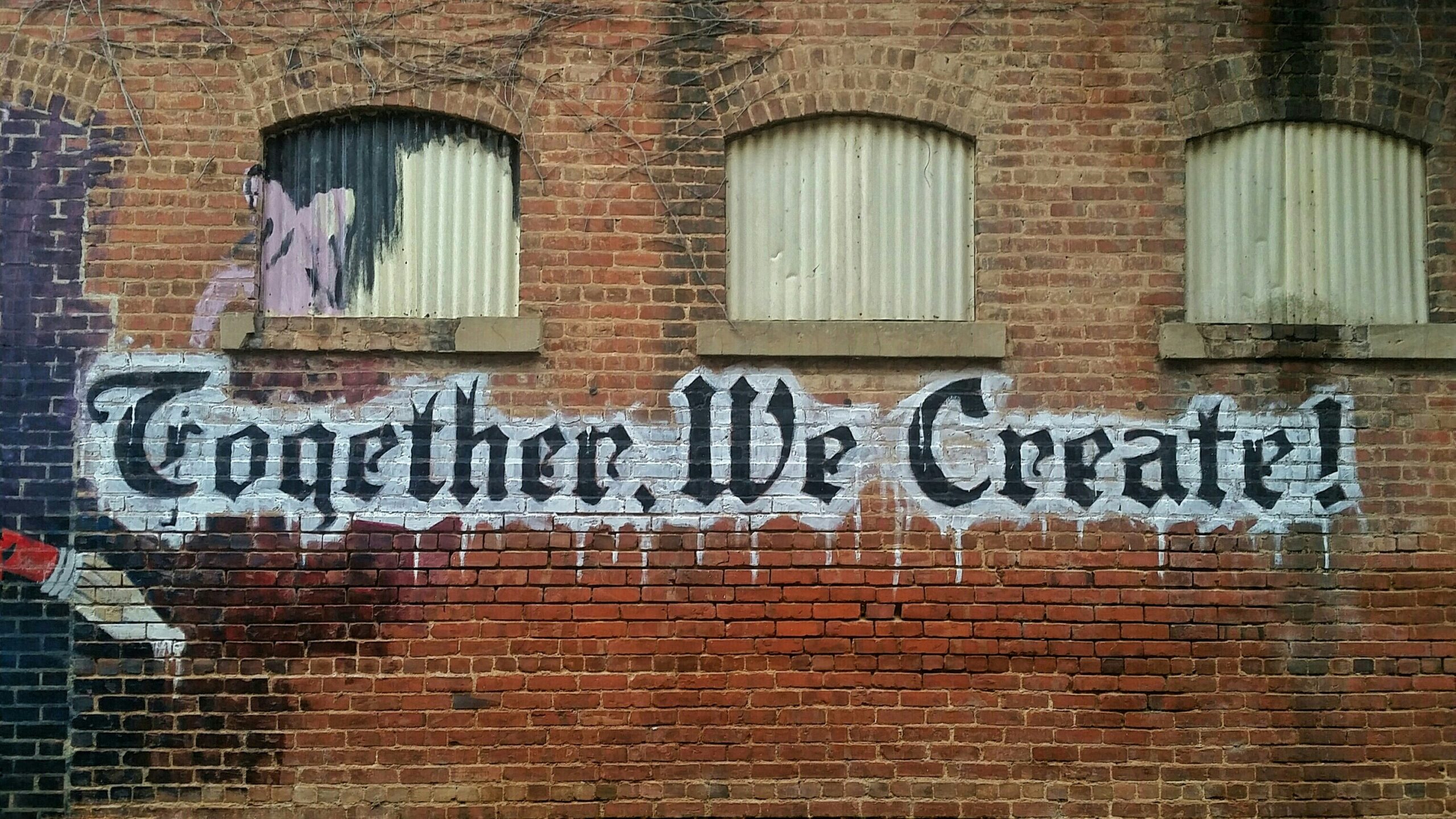 grafitti spelling 'together we create' on a brick red wall