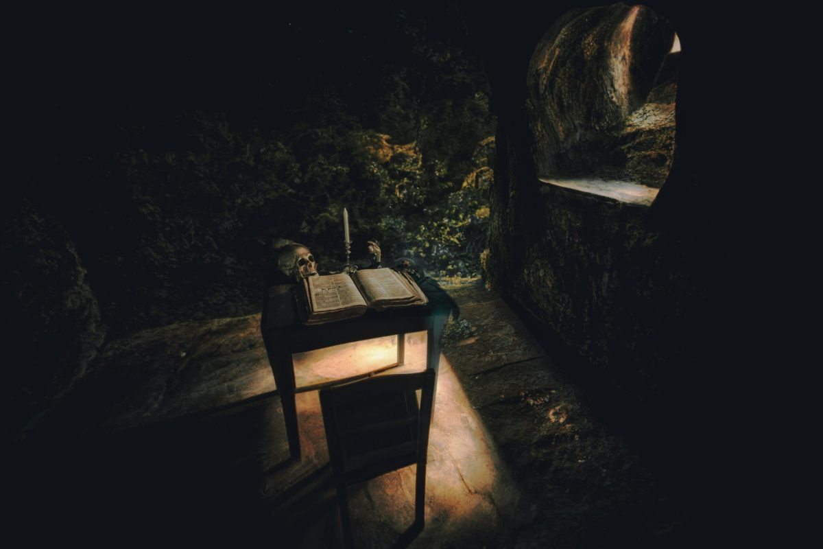 The picture illustrates a dark scene with table. A warm yellow light filtering in from a window on the right illuminates a book that sits on the table.