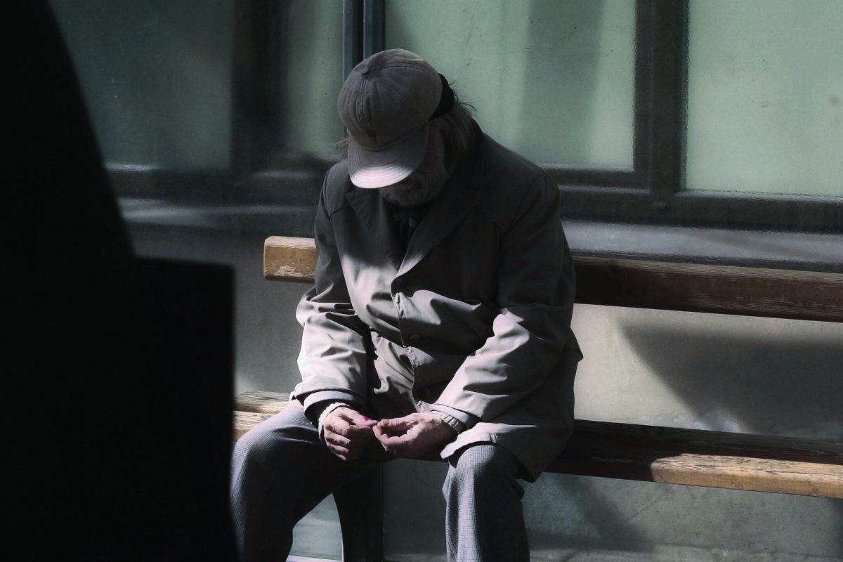 elderly man sitting on a bench alone, with dark shadows being cast on him. ageing population needs our help.